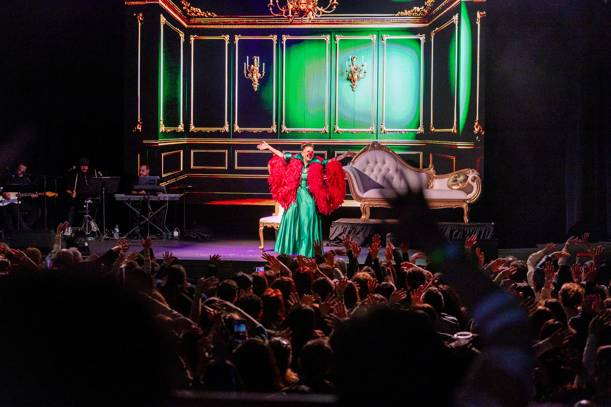 Artist performing in an elaborate green and gold stage set, crowd with hands raised at a LIVEST show.